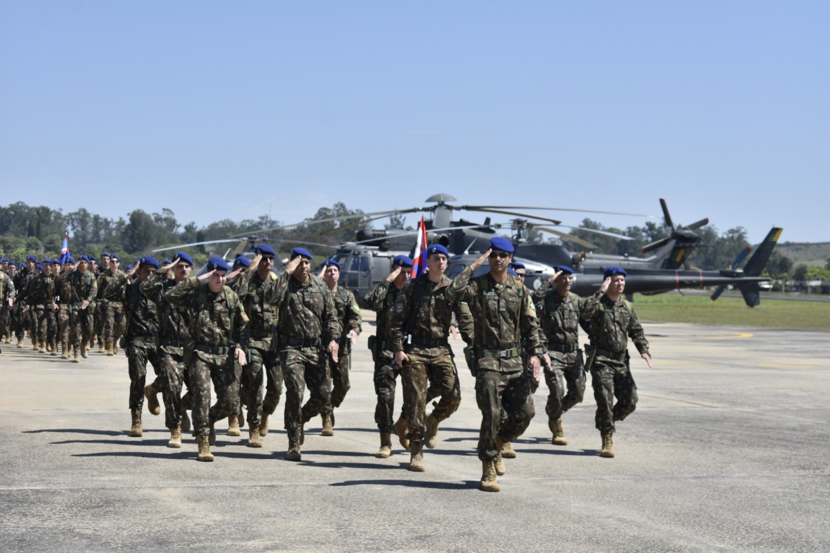 Militares da Aviação do Exército marcham em pista com helicópteros alinhados ao fundo